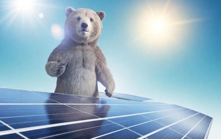Ein Erklärbär steht auf Solarpanelen vor einem sonnigen Himmel.