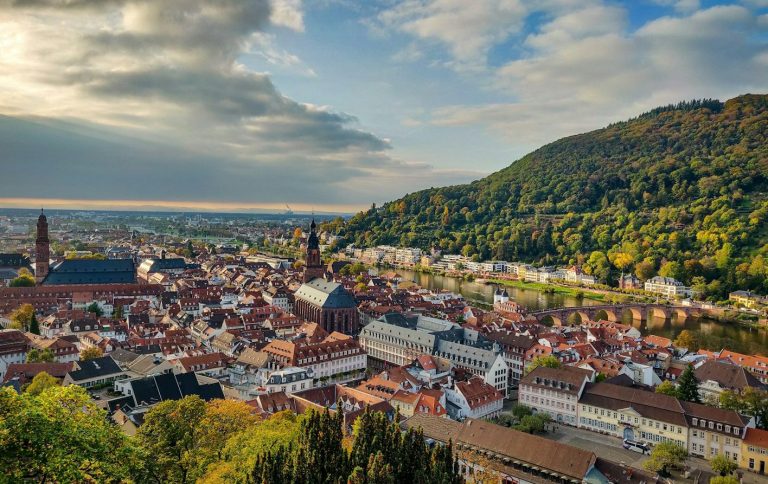 Panoramablick auf Heidelberg mit historischem Stadtzentrum und grünen Hügeln im Hintergrund.